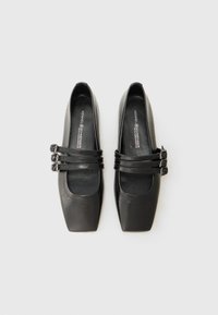 Chaussures en cuir noir à bout carré avec trois sangles réglables à boucles à l'avant ; texture lisse et semelles intérieures rembourrées.
