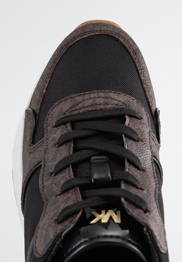 Baskets noires avec un dessus texturé marron, lacets noirs et semelle blanche. Un logo doré est visible sur le côté.