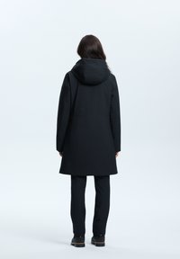 Musta vedenpitävä parka, jossa on huppu, suora leikkaus ja pitkät hihat. Minimalistinen yksityiskohtaisuus ja sileä pinta.