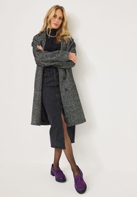 Grey textured coat with large buttons, paired with a black skirt featuring a side slit. Worn with purple loafers and black tights.