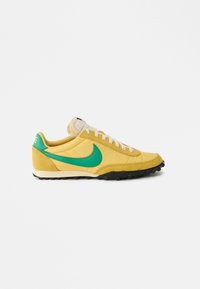 Yellow sneaker with green accents, textured fabric, cushioned collar, white laces, and black rubber sole featuring traction details.