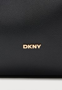 Čierna kožená taška s textúrovaným povrchom, výrazným tvarom a zlatým akcentom loga "DKNY".