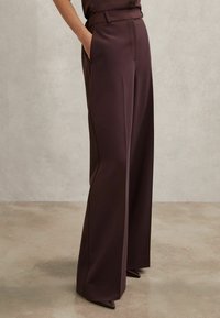 Bő szárú nadrág mély sötétlila anyagból, magas derékkal, sima textúrával és szabott fazonú oldalzsebekkel.