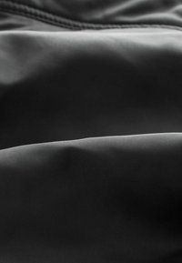 Sanft schwarzer Stoff mit dezenten Falten, die weiche Wellen und sanfte Highlights auf der strukturierten Oberfläche erzeugen.