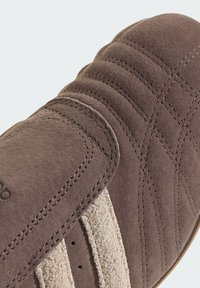 Brown suede shoe featuring a quilted design, light-colored suede accents, and two perforated stripes. Rounded toe and stitched detailing present.