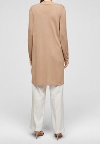 Beige stickad långtröja med rak skärning, ribbad textur och långa ärmar, kombinerad med vita vida byxor och ljusbruna klackar.