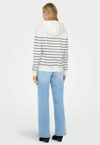 Biała bluza z kapturem i czarnymi poziomymi paskami, z elastycznymi mankietami, w połączeniu z jasnoniebieskimi szerokimi spodniami dżinsowymi.