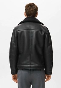 Chaqueta de cuero negro con cuello de borreguito, que presenta detalles cosidos y un ajuste entallado. La parte trasera es lisa con un diseño limpio.