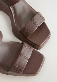 Brown platform sandals feature wide straps with stitched detailing and a textured wedge sole, showcasing a modern and stylish design.