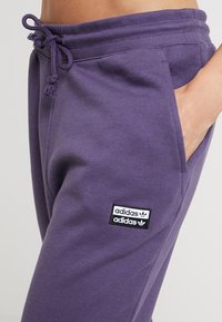 Lila bomullssweatpants med elastisk midja och snörning. Har en svart och vit Adidas-logotyp på framsidan av fickområdet.