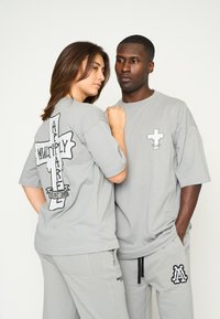 Camisetas de algodón de corte grande en gris con diseños gráficos: una tiene una cruz grande en la parte posterior y una cruz más pequeña en la parte delantera.
