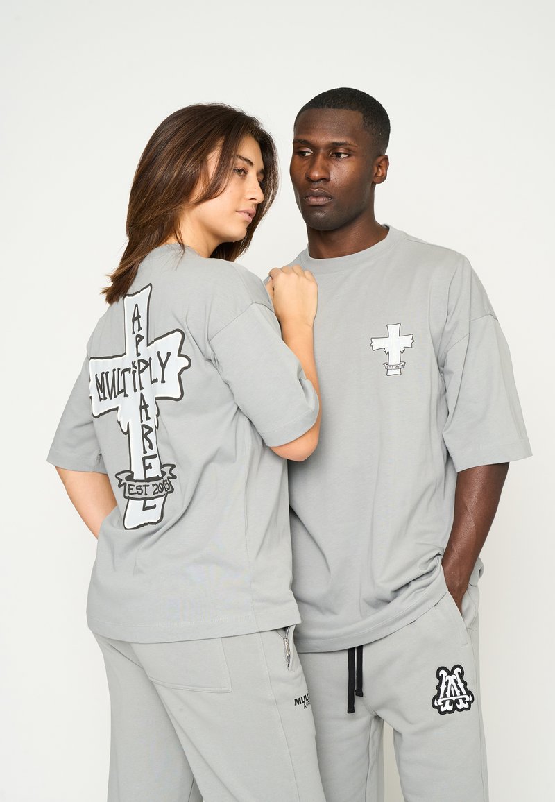 Grå oversized bomull t-shirts med grafiska mönster: en har ett stort kors på ryggen och ett mindre kors på framsidan.