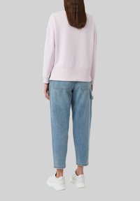 Jasnoróżowy sweatshirt z opuszczonymi ramionami, ribbowanymi mankietami i dolnym wykończeniem, w zestawieniu z niebieskimi jeansami o wysokim stanie i białymi sneakersami.