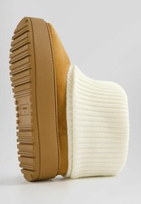 Bottine en daim marron avec un revers en tricot crème côtelé, dotée d'une semelle en caoutchouc texturée et d'un motif de bande de roulement horizontal épais.