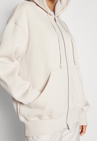 Ljusbeige zip-up hoodie med en rymlig passform, justerbar dragkedja i huven, stora framfickor och ribbade ärmslut och nederkant. Slät bomullsblandning.