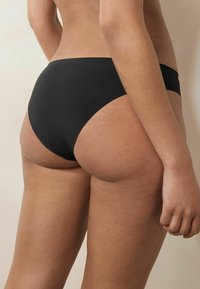Czarny dół bikini wykonany z gładkiego materiału o wysokim kroju. Minimalne detale szwów; brak dodatkowych wzorów lub elementów metalowych.