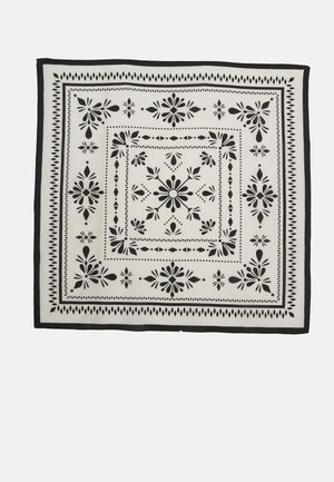 Firkantet stof med symmetriske blomster- og geometriske mønstre i sort og hvid, arrangeret i koncentriske kanter.