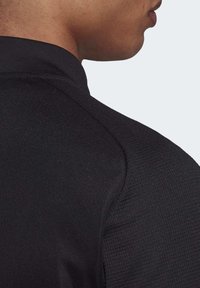 Zwarte sportshirt met een gestructureerde stof, een hoge kraag en gladde naden, die een slank en getailleerd ontwerp laat zien.