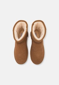 Brown suede ankle boots with a soft cream lining, rounded toe, and adjustable strap detail at the ankle. Flat sole for comfort.