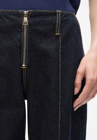 Donkerblauwe denim broek met een rits aan de voorkant, verstevigde stiksels en een rechte snit. Glad textuur met gele contraststiksel.details.