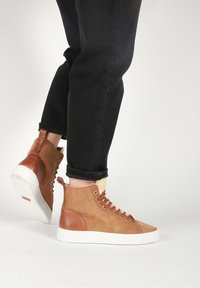 Ruske nahkaskinnsneakersit, joissa on samettiset yksityiskohdat, valkoinen kumipohja ja nauhakiinnitys. Näkyvissä on teksturoitu pinta ja pehmeä vuori.