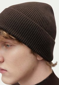 Brun ribbad stickad mössa, närbild, med en mjuk textur och sömlös design, placerad tätt på huvudet.