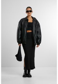 Svart skinn bomberjakke over en svart crop topp og en elegant svart maxiskjørt med sideslisse. Svart platåstøvler og en liten svart veske.