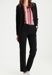 Czarna, dopasowana marynarka na kolorowej, paskowanej bluzce, w zestawieniu z czarnymi spodniami i białymi trampkami. Skupienie na czystych liniach i ostrym kroju.