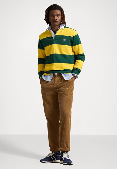 Groen en gele gestreepte rugbyshirt met een kraag, gecombineerd met een paarse corduroypantalon en marineblauwe sportschoenen. Heeft een gelaagde uitstraling.