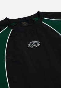 Zwarte lichtgewicht T-shirt met groene paneelaccenten, witte piping en een ronde logopatch op de borst, met een ronde halslijn.