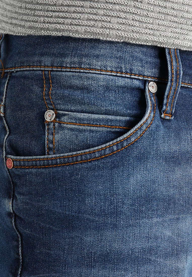 Blaue Denim-Jeans mit orangefarbener Naht, ausgestattet mit einer Vordertasche und Metallknopfdetails. Die Textur ist glatt mit einem leicht verblassten Finish.