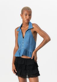 Denim top na halter z globokim V-izrezom, gumbastim sprednjim delom in peplum obrobjem. Siva modra barva, ima kontrastno šivanje in sproščen kroj.