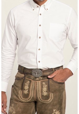 Homme portant une chemise blanche boutonnée rentrée dans un lederhosen en cuir marron brodé avec une boucle de ceinture argentée décorative.