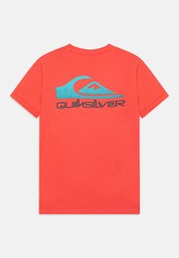 Červené bavlněné tričko s modrým grafickým designem vlny a textem "Quiksilver" v černé barvě, krátké rukávy a standardní střih.