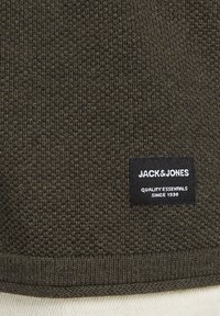 Donkergroene getextureerde gebreide stof met een zwart label waarop "JACK & JONES QUALITY ESSENTIALS SINCE 1990" staat, aan de zoom.