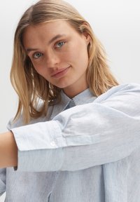 Light blue striped collared shirt with button cuffs, featuring a relaxed fit and soft texture, highlighting subtle vertical lines.