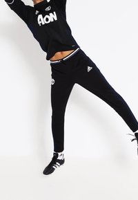 Musta urheiluasu, joka koostuu pitkähihasalaisesta paidasta, jossa on "AON"-logo, sekä mustista housuista, joissa on valkoisia yksityiskohtia. Asusteena mustat ja valkoiset nappakengät.