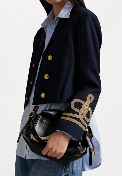 Navy cropped blazer with gold buttons, detailed braiding on sleeve; light blue collared shirt underneath; black leather handbag with curved handle.
