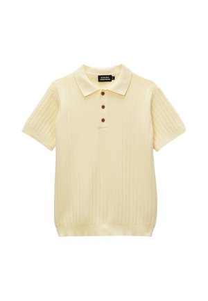 Polo en maille crème à manches courtes avec trois boutons marron et un motif chevron texturé sur fond blanc.