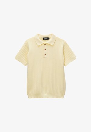 Polo en maille crème à manches courtes avec trois boutons marron et un motif chevron texturé sur fond blanc.