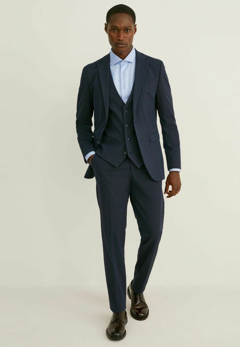 Marinblå tre-delad kostym med ett randigt mönster, bestående av en skräddarsydd kavaj, väst och avsmalnande byxor; matchas med en ljusblå skjorta.