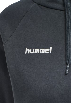 Close-up van een donkergrijze hoodie met wit "hummel" logo op de borst en een gevlochten trekkoord aan de rechterkant.