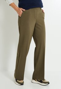 Pantalons larges vert olive en tissu lisse et extensible. Équipés de poches avant et d'une taille ajustée. Associés à des chaussures de sport multicolores.