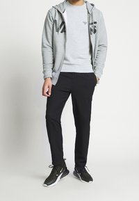 Sudadera gris con cremallera y texto gráfico negro, combinada con un sudadera gris a juego, pantalones negros ajustados y zapatillas deportivas negras.