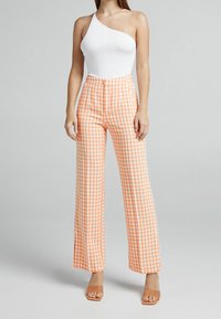 Vitt one-shoulder bodysuit kombinerat med högmidjade, vida byxor i orange och vit rutig; mjukt tyg, avslappnad passform.