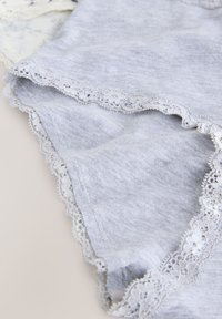 Gråt stof med en blød tekstur har fin hvid blonderkant langs kanterne, hvilket skaber en subtil kontrast i design og detaljer.