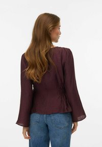 Langærmet bluse i bordeaux krøllet stof med en tætsiddende overkrop og løstsiddende klokkeærmer. Teksturen er let gennemsigtig med diskrete detaljer.