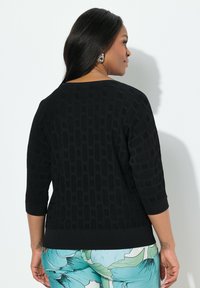 Schwarzer strukturierter Pullover mit 3/4-Ärmeln und lockerem Schnitt, der ein sich wiederholendes geometrisches Muster sowie gerippte Bündchen und Saum aufweist.
