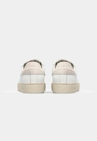 Sneakers bianchi in pelle con inserto in suede sul tallone, punta tonda e suola in gomma color crema. Design minimalista con una texture liscia sulla tomaia.
