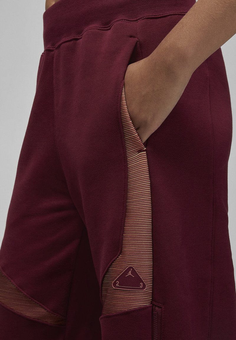 Bordeauxfarbene Jogger-Hosen mit einem gerippten Taschenakzent in einem helleren Farbton, ausgestattet mit einem dreieckigen Logopatch und einem schlanken Schnitt.